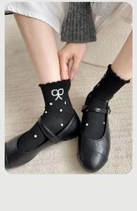 Close-up of black knit crew socks with white bow embroidery and polka dots on rug