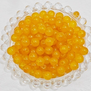 Macro detail of translucent orange glass beads for DIY jewelry making in a glass bowl