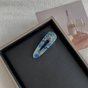 Close-up of a rectangular hair clip with blue and gold marble texture on a black display tray
