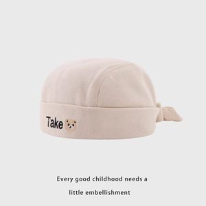 Détail d'un bonnet bébé en coton côtelé beige avec broderie et écusson d'ours