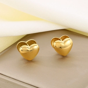 Macro detail of polished gold-finished titanium steel heart earrings on silk fabric