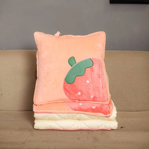 Detail of plush strawberry pattern pillow blanket unfolded on a beige sofa