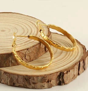Nahaufnahme goldener Creolen mit Herzprägung auf einer natürlichen Holzscheibe