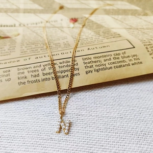 Close-up of gold-plated titanium steel necklace with pearl-inlaid letter N pendant.