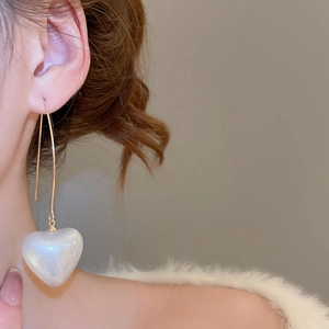 Close-up of a large pearl heart pendant on a gold hook earring worn by a model