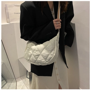 Close-up of a quilted ivory crescent bag featuring a wide shoulder strap on a model