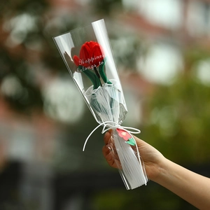 Handmade red crochet tulip flower in a transparent gift bag held in a garden