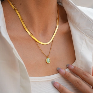 Détail d'un collier doré multicouche avec chaîne serpent et pendentif en œil-de-chat