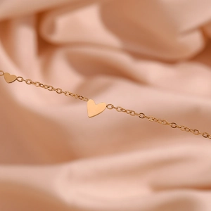 Close-up of elegant gold heart pendants on a fine chain over pink silk fabric