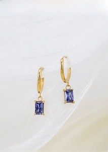 Detailed close-up of gold titanium steel earrings with blue rectangular zircon on soft tulle