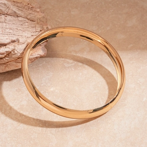 Detailed view of three polished gold geometric bangles on a warm stone background