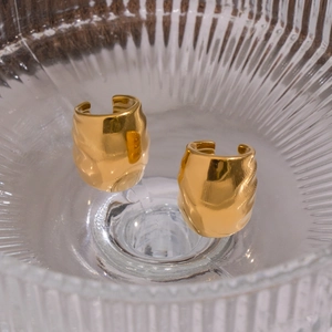Polished wavy gold geometric ear cuffs displayed in a textured glass bowl with high shine