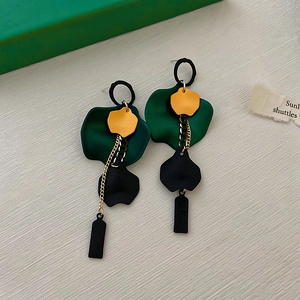 Detailed view of green and yellow floral earrings with black rectangle tassels and gold chains