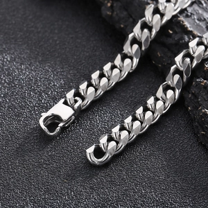 Close-up of a silver Cuban link necklace with a secure lobster clasp on a dark surface