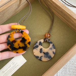 Macro detail of tortoiseshell resin pendants on a woven cord with wooden bead accents