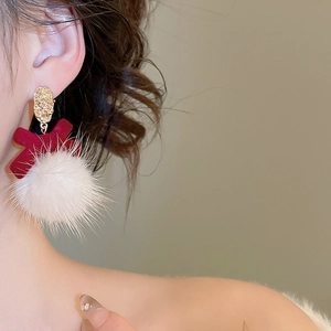 Detail of velvet red bow and fluffy white pompom earring on a model ear