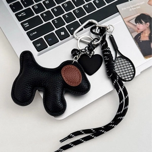 Black leather dog bag charm with brown ears and tennis racket on laptop keyboard