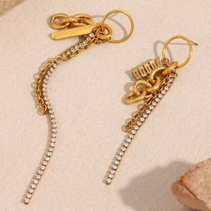 Détail de boucles d'oreilles à pompons plaquées or 18 carats avec zircons et plaque gravée