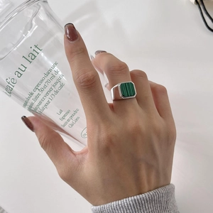 Detail of square green malachite ring in 925 silver on hand holding a glass cup