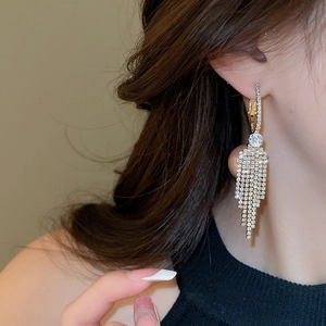 Close-up of sparkling long tassel earrings with pavé zircons on a golden base