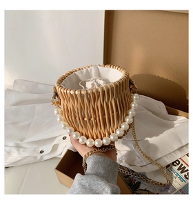 Detail of woven straw bucket bag with large pearl handle and gold chain strap