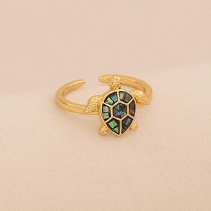 Detailed close-up of golden turtle ring featuring iridescent shell inlay on beige fabric