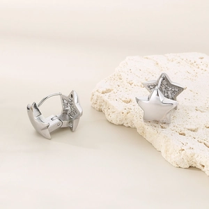 Macro shot of silver star-shaped hoop earrings resting on a white textured stone
