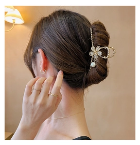 Détail d'une pince à cheveux dorée en métal avec fleur en cristal et perle sur un mannequin