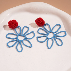 Détail de boucles d'oreilles rose rouge et marguerite bleue sur un plateau céramique