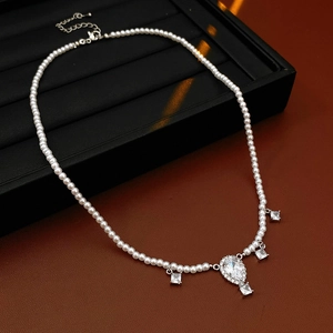 Detail of beaded pearl necklace with silver drop pendant and clear gemstones on black tray