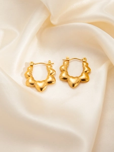 Macro shot of gold heart hoop earrings featuring polished metallic texture on silk fabric