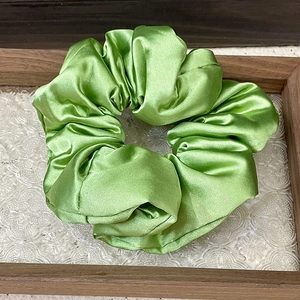 Detailed view of a green satin scrunchie on a vintage glass and wood display tray
