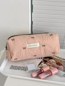 Detail of pink quilted makeup bag with bow embroidery and zipper closure in a tray