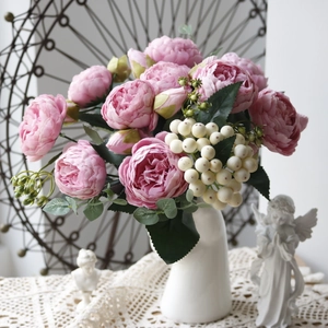 Pink artificial peony and rose bouquet in a white vase with decorative angel statues