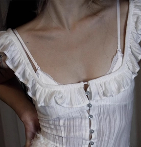 Detailed macro view of white ruffled lace cardigan with blue buttons and pleated fabric