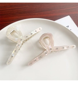 Macro shot of two pearlescent white hair clips with rhinestones on a ceramic dish