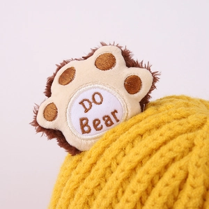 Close-up of ginger yellow knit hat with cute bear paw plush decor and DO Bear embroidery