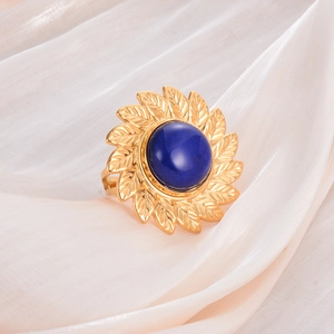 Detailed close-up of golden leaf-shaped ring with a large blue gemstone on silk fabric