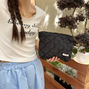 Close-up of black quilted pouch with diamond texture and small woven label in a casual setting