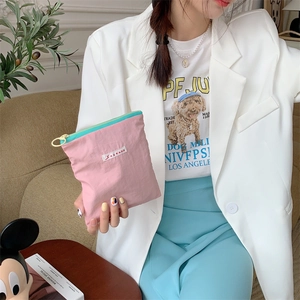 Detail of pink macaroon makeup bag with blue zipper held by a model in a casual setting