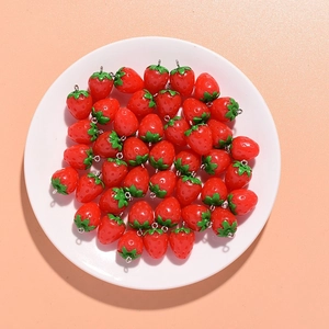 Top view of vibrant red resin strawberry pendants with green leaves in a white ceramic dish