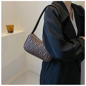Detailed texture of brown pleated leather underarm bag worn by a model in a black coat