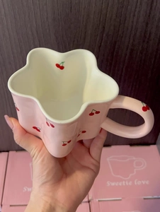 Close-up of pink petal-shaped ceramic mug with cherry patterns and wave-rim detail