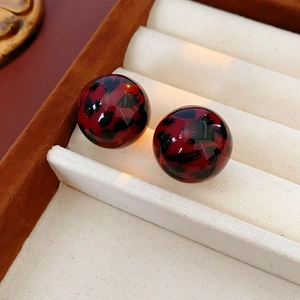 Detail view of round leopard print stud earrings in deep red resin on beige velvet tray