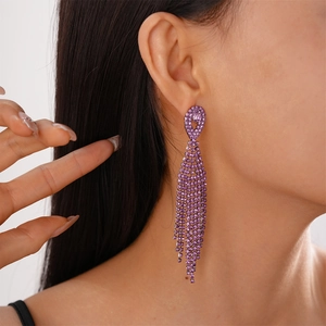 Close-up of elegant long tassel earrings with sparkling purple rhinestones worn by a model