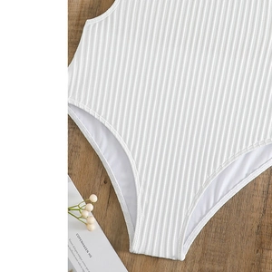 Detail of white ribbed one-piece swimsuit featuring high-cut design on wood surface