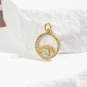 Macro shot of gold Evil Eye pendant with white shell inlay and sparkling zirconia stones