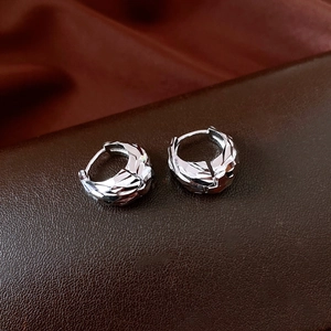 Macro shot of silver pleated U-shaped hoop earrings with geometric facets on dark fabric