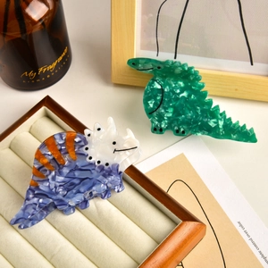 Detailed view of green crocodile and blue triceratops acetate hair claws on a wooden tray