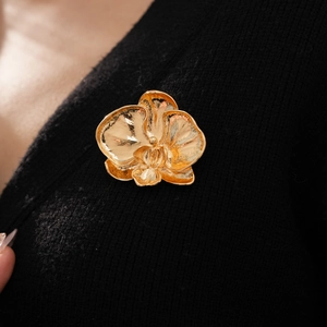 Detailed macro view of golden orchid brooch with matte metallic petals on black knitwear